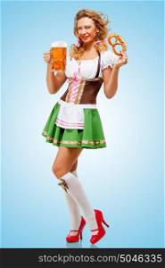 Young sexy Oktoberfest woman wearing a traditional Bavarian dress dirndl posing with a pretzel and beer mug in hands on blue background.