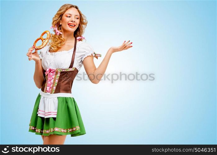 Young sexy Oktoberfest woman wearing a traditional Bavarian dress dirndl posing with a soft salty pretzel on blue background.