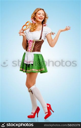 Young sexy Oktoberfest woman wearing a traditional Bavarian dress dirndl posing with a soft salty pretzel on blue background.