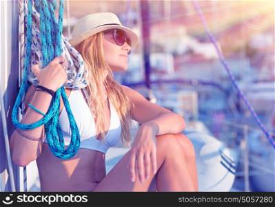 Young sexy sailor girl relaxing on sailboat, holding rope, enjoying sea cruise, active lifestyle, female in mild sunset light, summer vacation concept