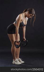 Young sexy woman exercising and lifting kettle bells.