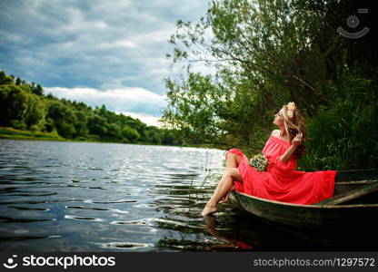 Young sexy woman in red dress on boat. The girl has a flower wreath on her head, relaxing and seiling on river. Fantasy art photography. Concept of female beauty, rest in the nature, and water travel. Young sexy woman in red dress on boat. The girl has a flower wreath on her head, relaxing and seiling on river. Fantasy art photography. Concept of female beauty, rest in the nature, and water travel.