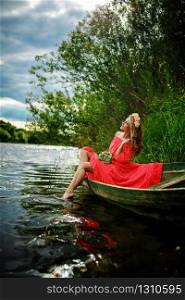 Young sexy woman in red dress on boat. The girl has a flower wreath on her head, relaxing and seiling on river. Young sexy woman in red dress on boat. The girl has a flower wreath on her head, relaxing and seiling on river.