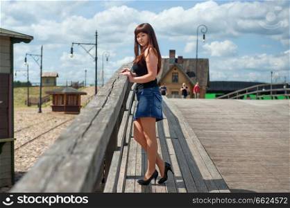Young, sexy  woman in short skirt stand on the old-time bridge. 