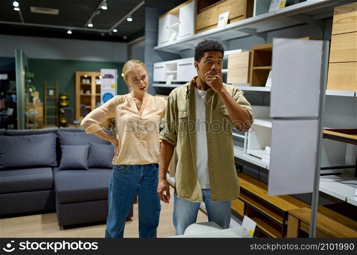 Young shocked married family couple buyer disappointed with expensive price in furniture store. Couple disappointed with price in furniture store