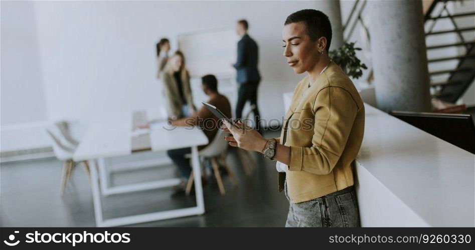 Young short hair business woman standing in the office and using digital tablet in front of her team