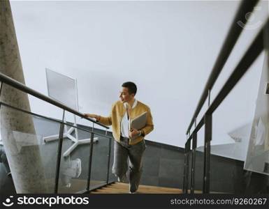 Young short hair business woman walking on the office stairs and holding laptop