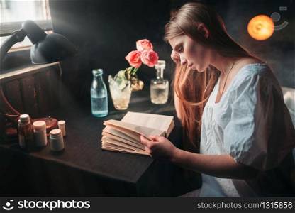 Young sick woman reading book at the hospital, drugs on the table. Illness of female patient in clinic, health recovery and treatment. Young sick woman reading book at the hospital