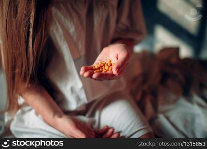 Young sick woman sitting on hospital bed with drugs in hand. Illness of female patient in clinic, health recovery and treatment. Sick woman sitting on hospital bed, drugs in hand