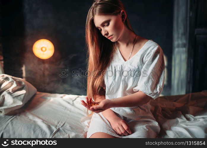 Young sick woman sitting on hospital bed with drugs in hand. Illness of female patient in clinic, health recovery and treatment. Sick woman sitting on hospital bed, drugs in hand