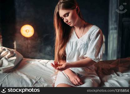 Young sick woman sitting on hospital bed with drugs in hand. Illness of female patient in clinic, health recovery and treatment. Sick woman sitting on hospital bed, drugs in hand