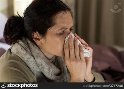 Young sick woman sneezing in tissue sweating from flu fever