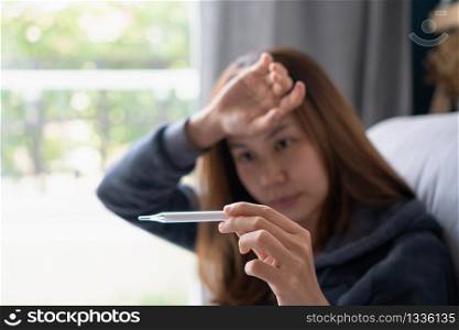 Young sick woman with fever checking her temperature with a thermometer at home. The concept of disease and ill