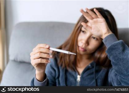 Young sick woman with fever checking her temperature with a thermometer at home. The concept of disease and ill