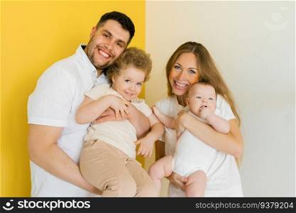 Young sincere family, where a happy father and mother hold their lovely children in their arms. Family photo shoot in the studio