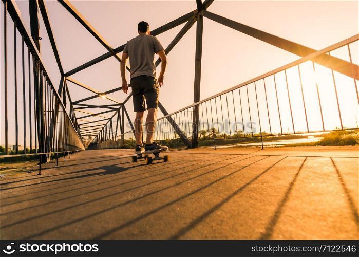 Young skateboarder speed through the pedestrian walkway Bridge at sunset.