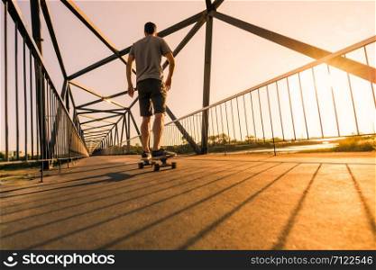 Young skateboarder speed through the pedestrian walkway Bridge at sunset.