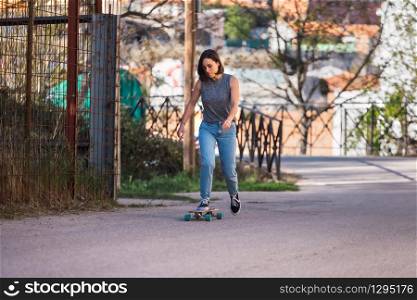 Young skater woman riding on her longboard in the village in casual wearing, freedom concept