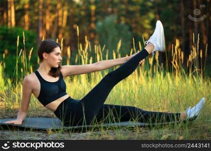 Young slender girl athlete performs an exercise in the park. Natural green background. Sunny day. Young slender girl athlete performs an exercise in park