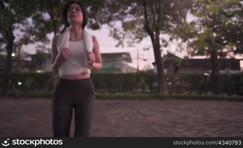 Young slim attractive black hair asian woman stretching body before exercising in evening at park, warming body up before exercise by raising knee up and moving mid body in evening twilight time