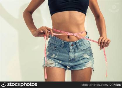 Young slim woman measures her waist by measuring tape after diet against white backgrounds. Concept of weight loss success.