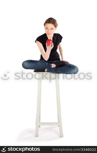Young slim woman sitting on stool and holding red apple against isolated white background