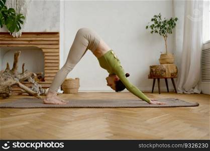 Young slim woman standing in Adho Mukha Svanasana yoga position engaged in stretching workout. Training at home for wellness and wellbeing. Young slim woman standing in Adho Mukha Svanasana yoga position