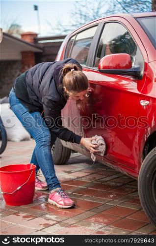 Young slim woman washing red car door with rug