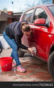 Young slim woman washing red car door with rug