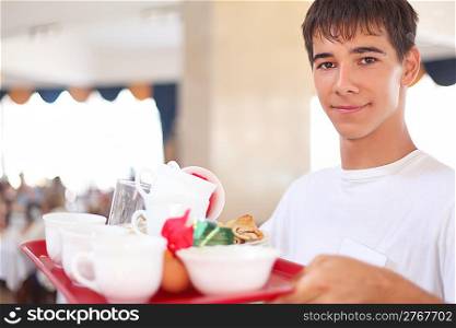 young smiling affable waiter keeps tray with dishes at restaurant
