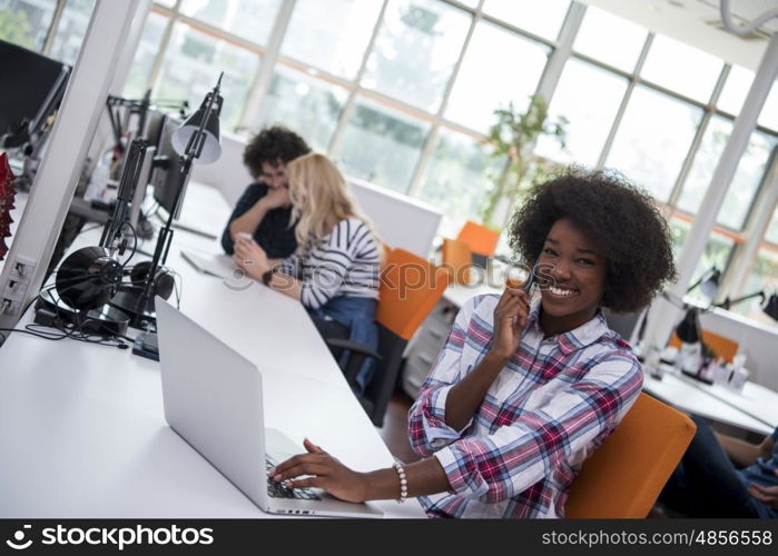 young smiling African American informal businesswoman working in the office with colleagues in the background