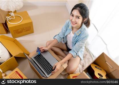 Young smiling asian customer woman holding credit card and payment with laptop. Portrait of happy asian girl looking camera at home in top view. Shoppinng and payment online technology concept.