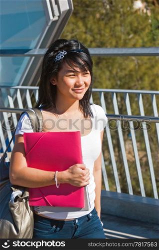 Young smiling Asian student holding a pink folder and wearing a tiara