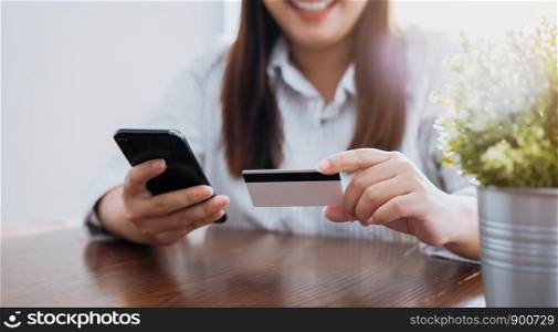 Young smiling Asian woman hand holding credit card and smartphone enter the payment code for the product. Pay online for convenience.