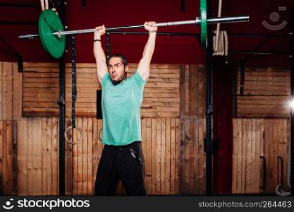 Young smiling athlete doing some weightlifting exercises with green t-shirt