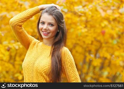 Young smiling brunette posing in autumn park on yellow trees background. Young brunette in autumn park