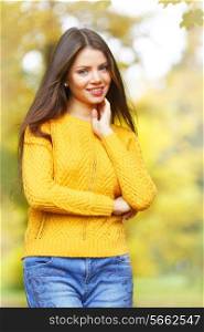 Young smiling brunette posing in autumn park on yellow trees background