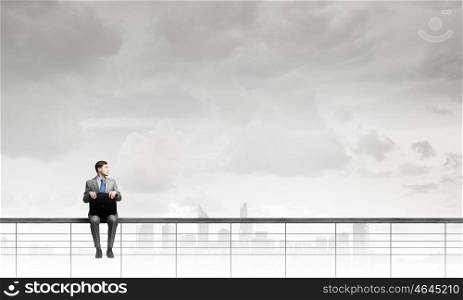 Young smiling businessman sitting with briefcase in hands. Businessman with suitcase