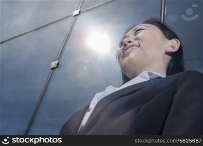Young smiling businesswoman outside in front of glass building, low angle view