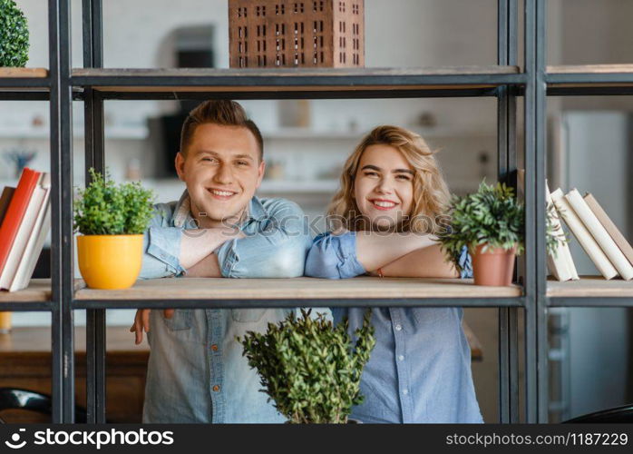 Young smiling couple at the shelf with home plants, florist hobby. Man and woman takes care and growing domestic flowers, gardening, botany lifestyle