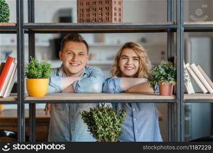 Young smiling couple at the shelf with home plants, florist hobby. Man and woman takes care and growing domestic flowers, gardening, botany lifestyle