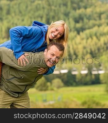 Young smiling couple having fun piggyback riding in the nature