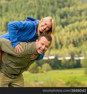 Young smiling couple having fun piggyback riding in the nature