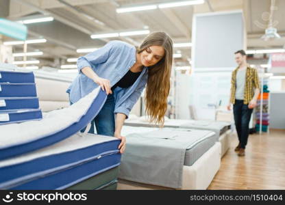 Young smiling couple in furniture store showroom. Man and woman looking samples for bedroom in shop, husband and wife buys goods for modern home interior. Young smiling couple in furniture store showroom