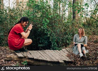 Young smiling couple of women reading a book and taking photos with old camera in the forest.