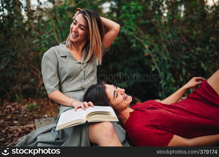 Young smiling couple of women wearing dresses reading a book and taking photos with old camera in the forest
