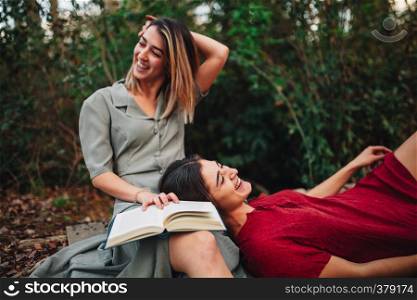 Young smiling couple of women wearing dresses reading a book and taking photos with old camera in the forest