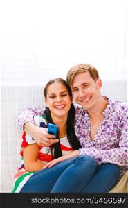Young smiling couple sitting on couch with mobile&#xA;