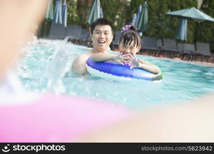 Young smiling family splashing and playing in the pool