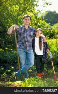 Young smiling father and daughter posing at garden with shovels